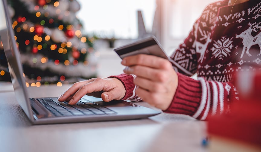 A woman holds a credit card while doing online holiday shopping