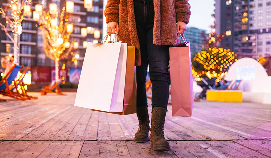 person holding shopping bags with holiday decorations in the background