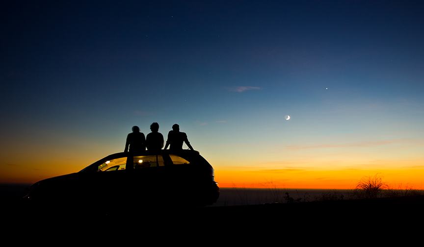 Friends sit on the roof of a car watching sunset.