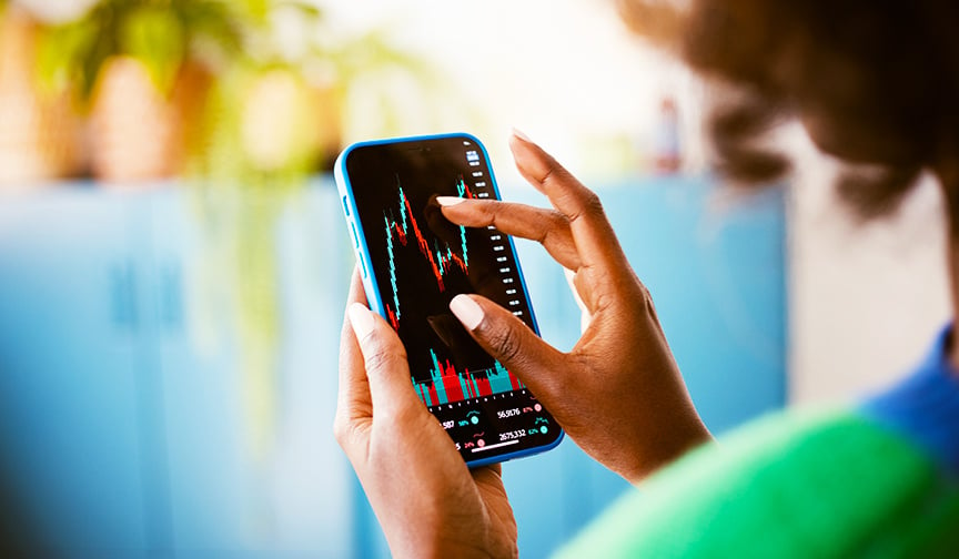 person in green shirt holding phone that shows stock charts