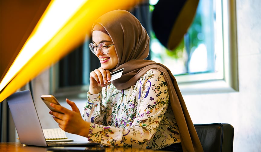 woman holding phone and credit card sitting in front of laptop