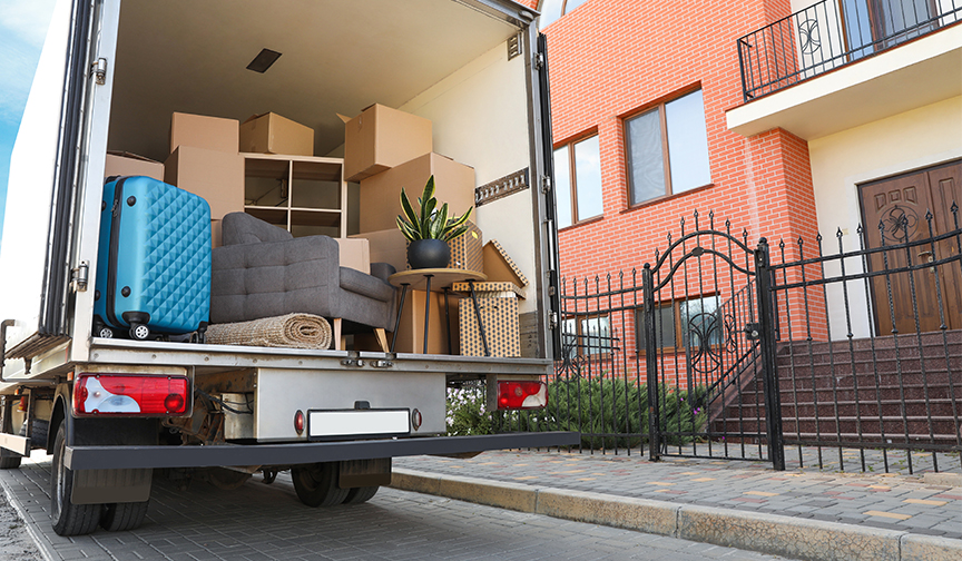 A moving truck full of boxes idles in front of an apartment building.