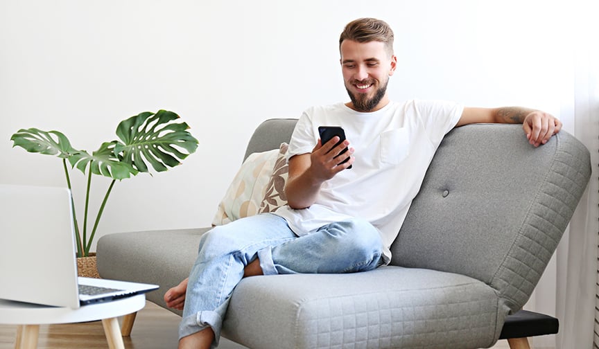 Smiling man sits on couch looking at cell phone