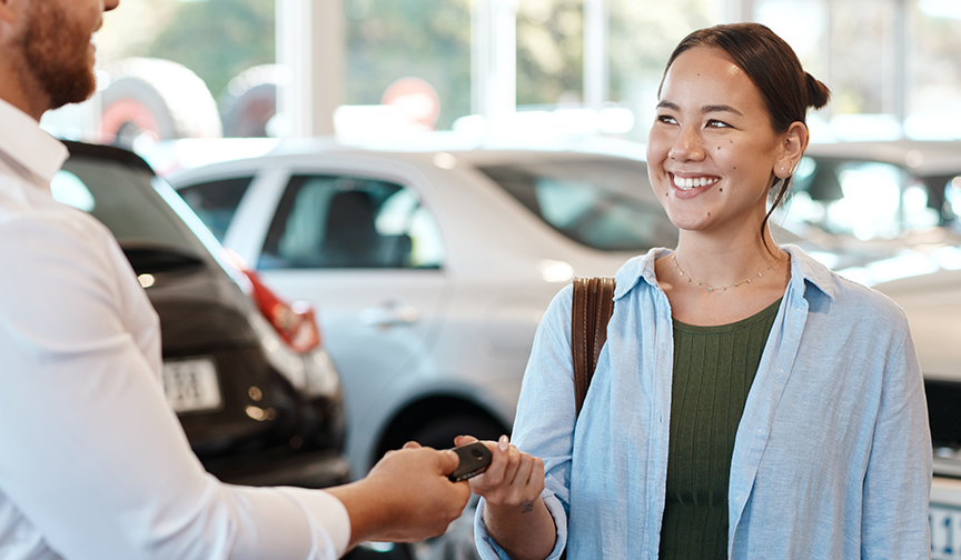 Car salesman hands young woman keys to a new car