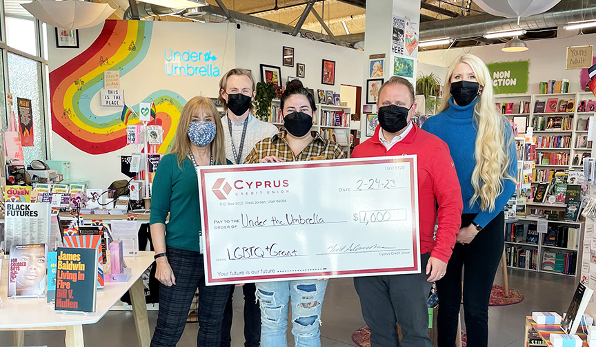 Kaitlyn Mahoney, owner of Under the Umbrella Bookstore, and Cyprus employees hold a large check for $1,000.